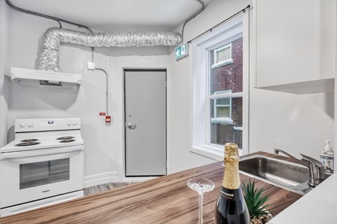 A kitchen with a stove, a sink, and a bottle of champagne on the counter.