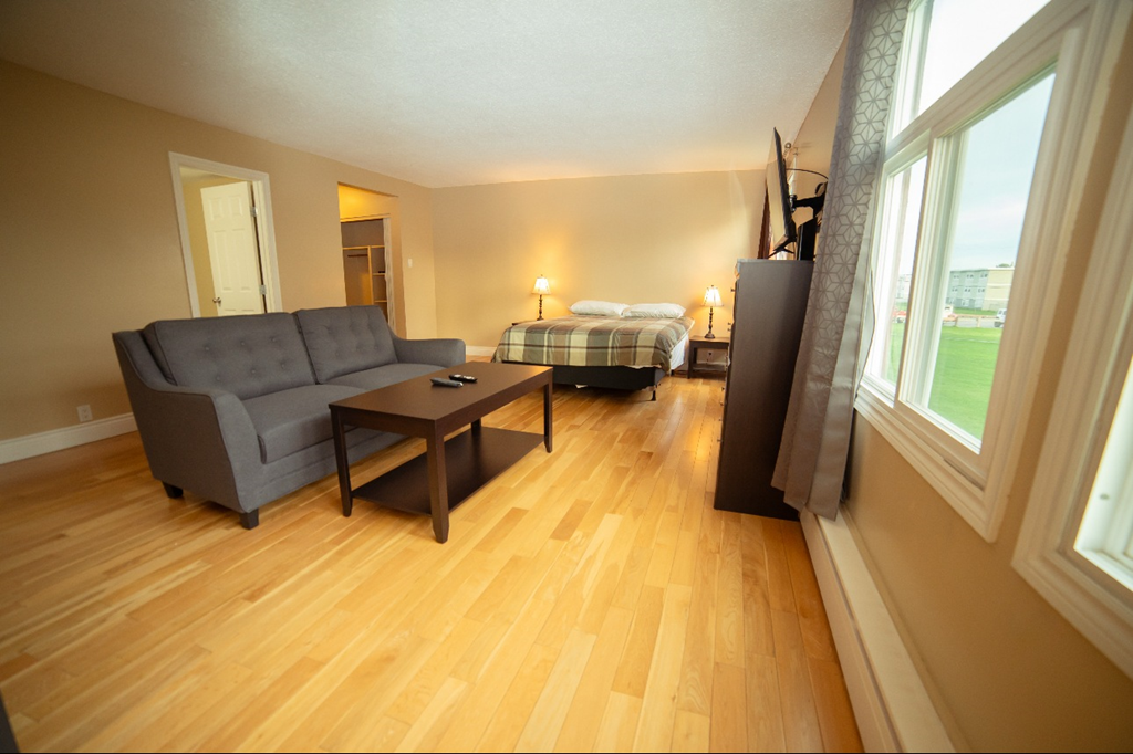 A living room with a grey couch and a bed in the background.