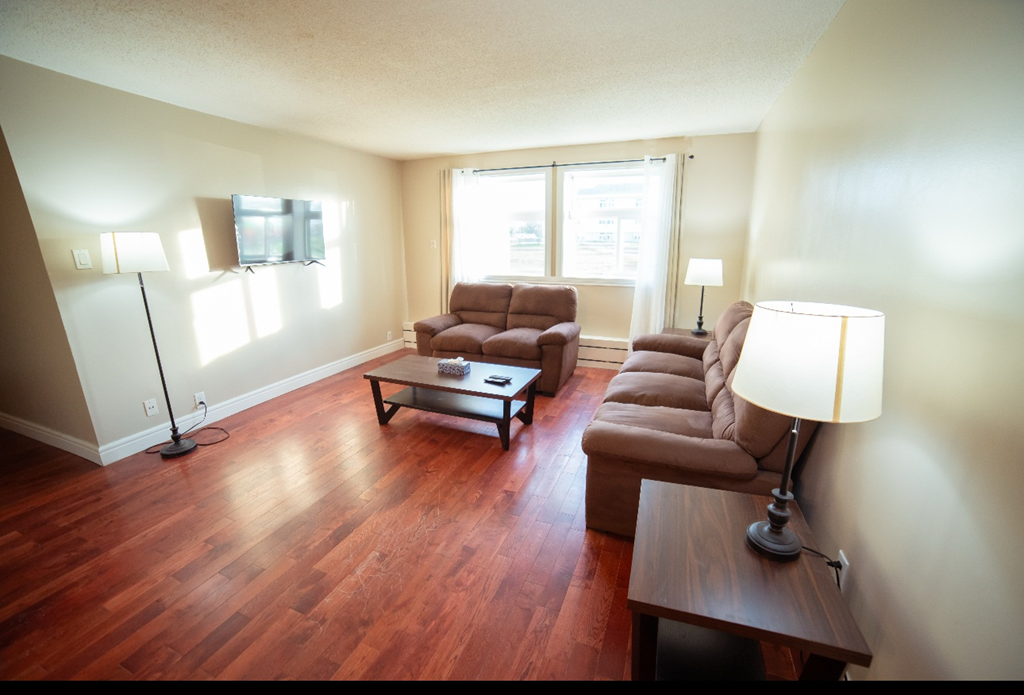 A living room with brown leather furniture and a wooden floor.