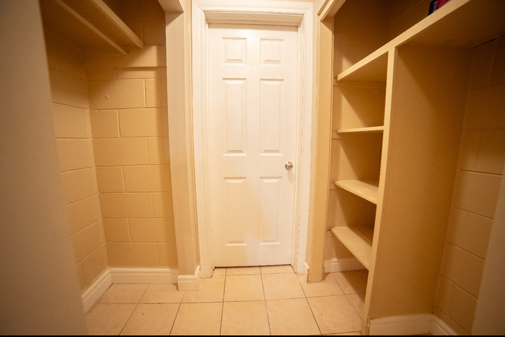 A white door is in a hallway with shelves on either side.