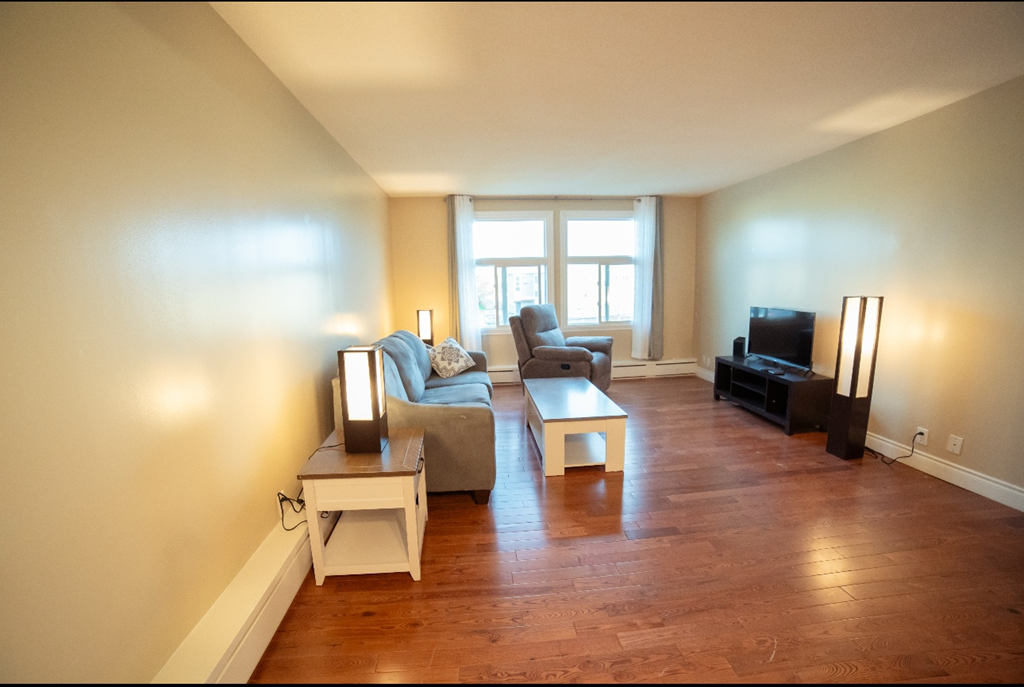 A living room with a grey couch, a white end table, a wooden coffee table, and a black television.
