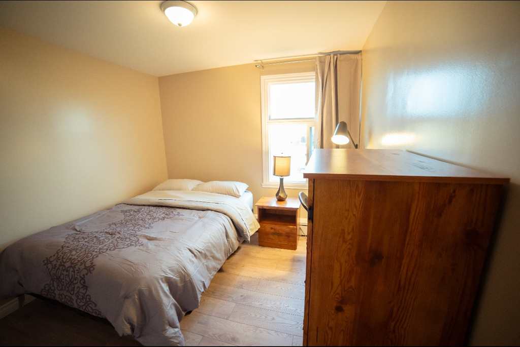 A bedroom with a bed, nightstand, and window.