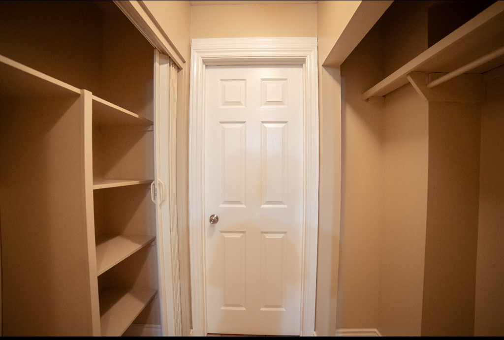 A white door is in a hallway with shelves on either side.