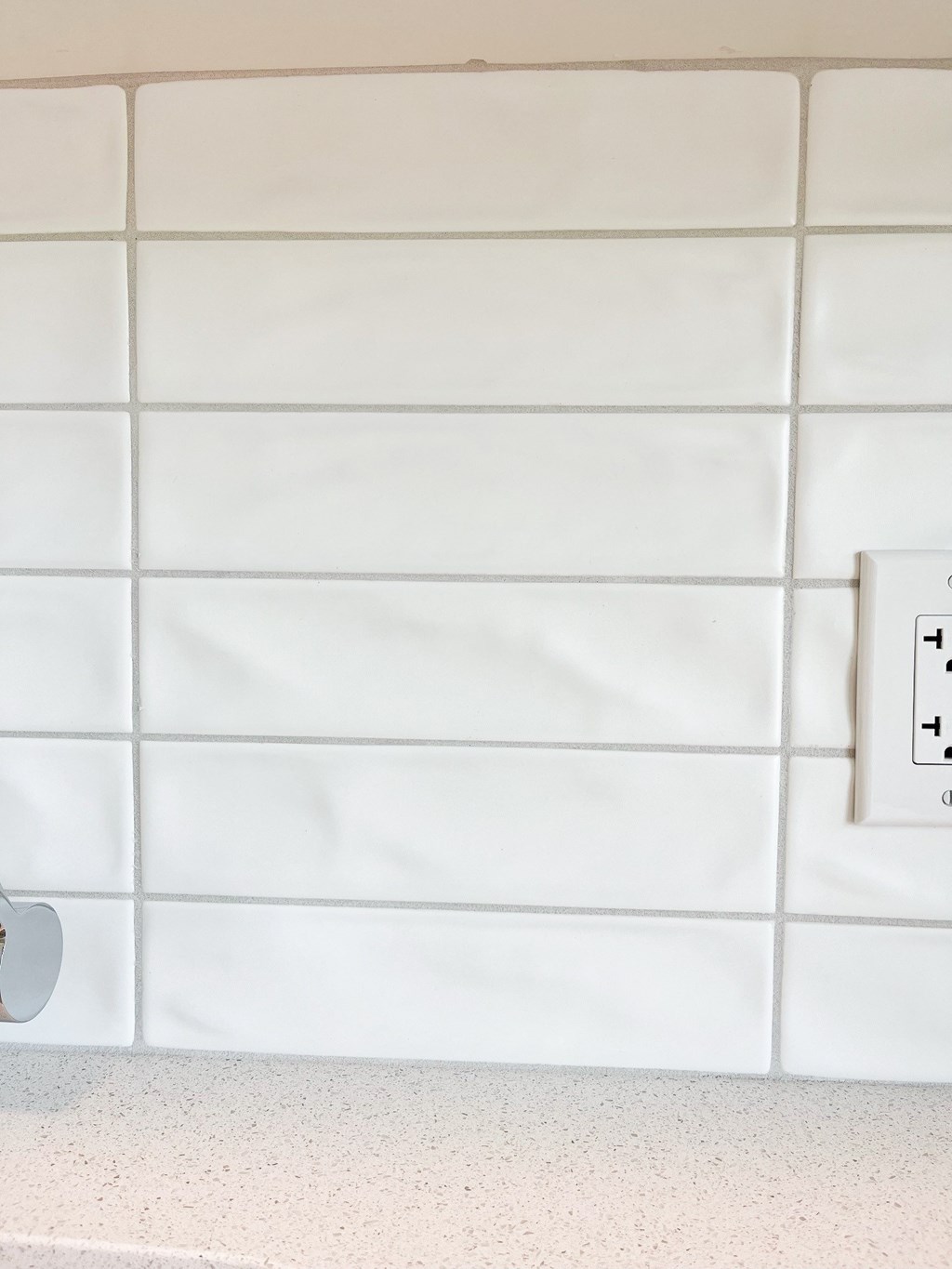 a white tiled wall with an electrical outlet and a light switch