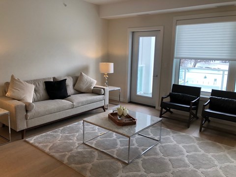 A living room with a grey couch, a glass coffee table, and a lamp.