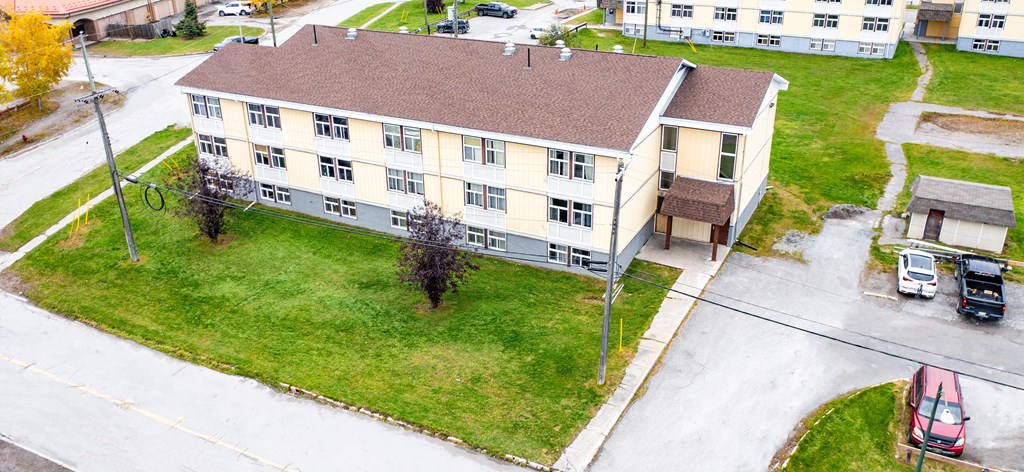 A large building with a brown roof is surrounded by a grassy area and a parking lot.