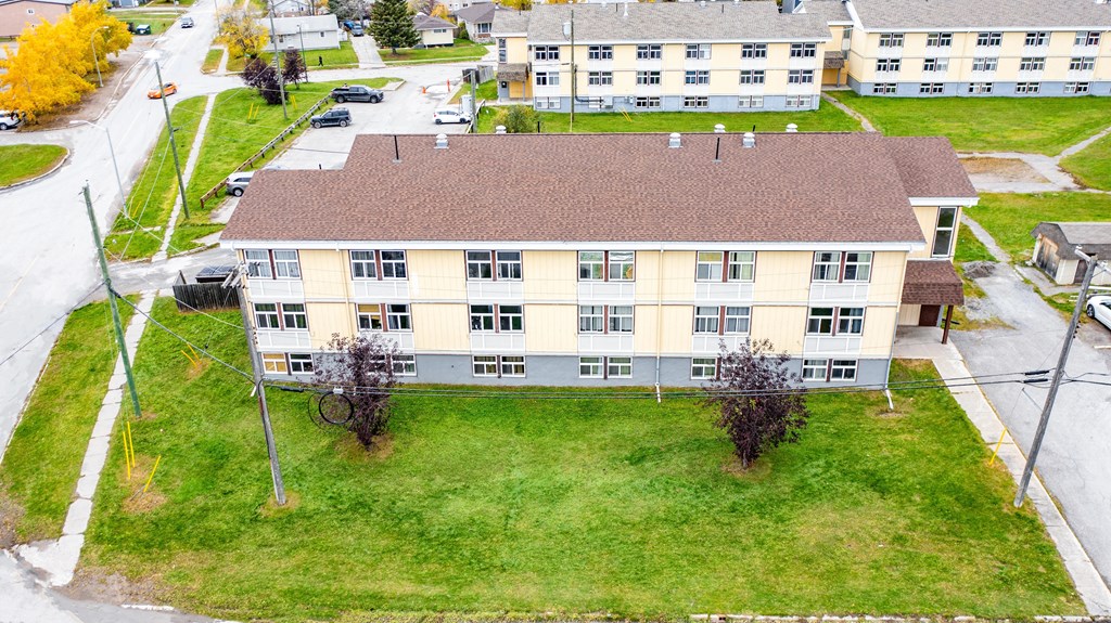 A large building with a brown roof is surrounded by a grassy area and a few trees.