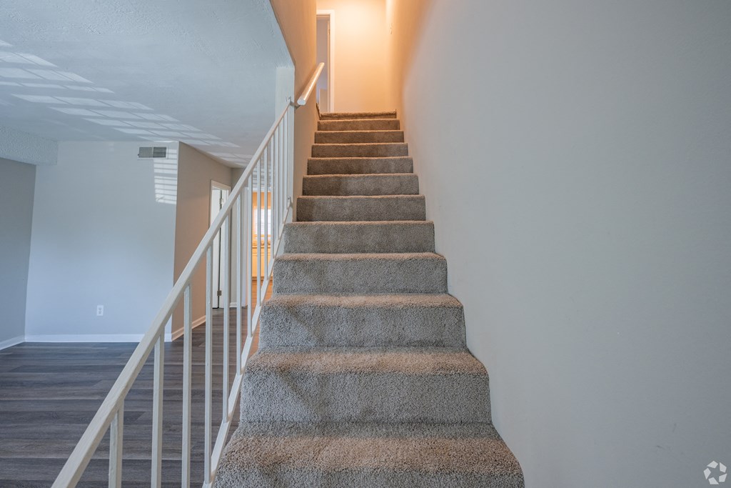 an image of a staircase in a house with white railings and carpeted stairs