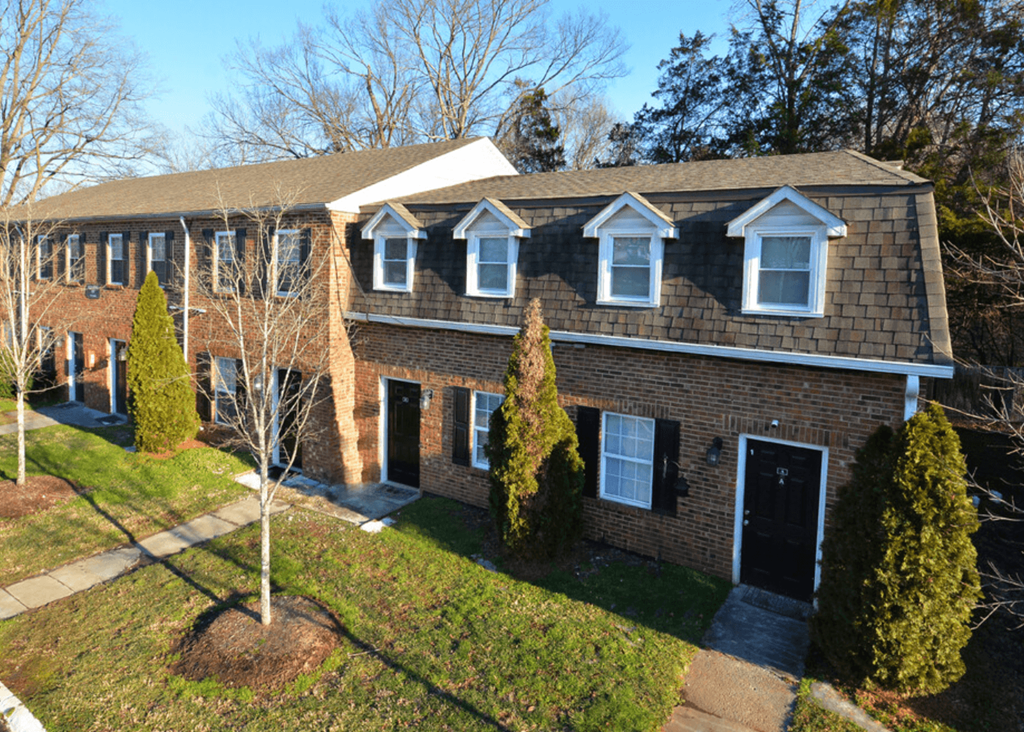 the front of a brick house with a lawn and trees