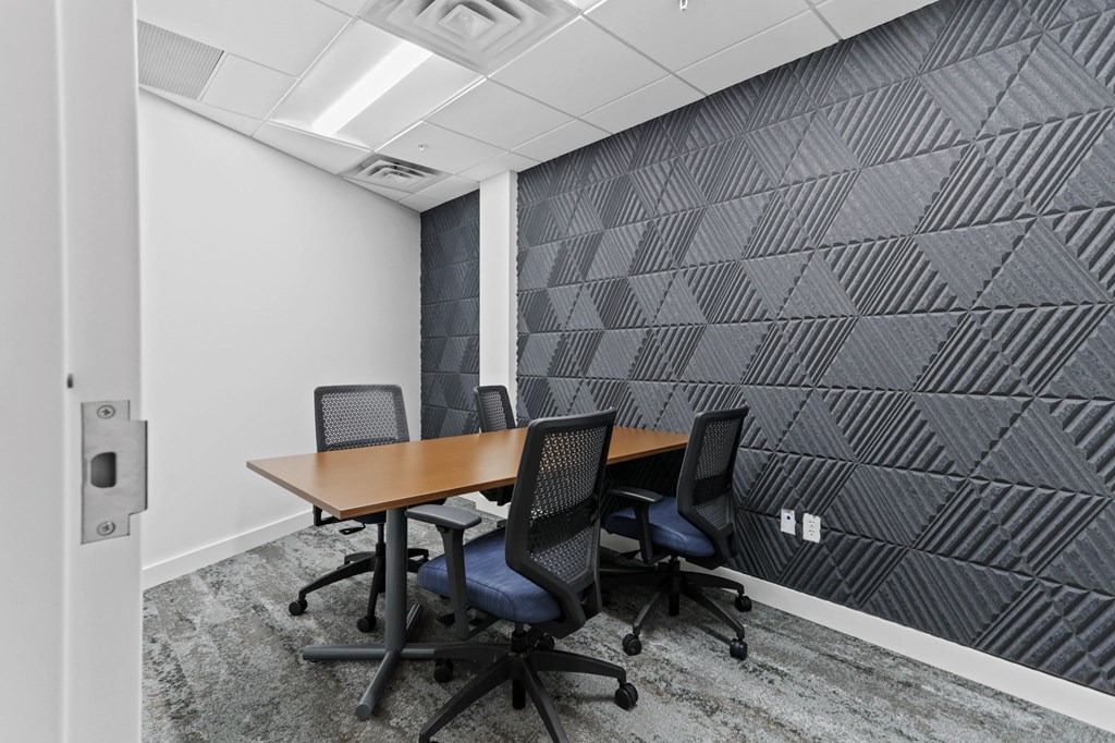 a small meeting room with a wooden table and four black chairs