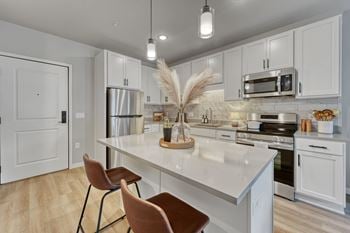 A kitchen with white cabinets and a white island with two chairs at Lochner Apartments, White Bear Lake, 55110
