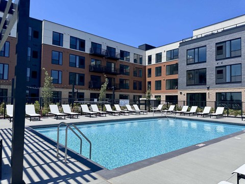 A pool surrounded by sun loungers in front of apartment buildings.