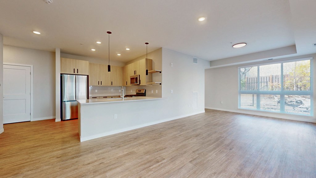 an empty living room with a kitchen and a large window