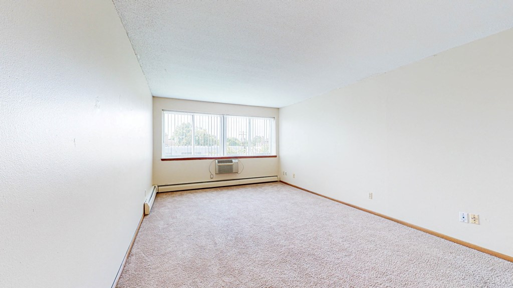 the living room of an apartment with carpet and a window