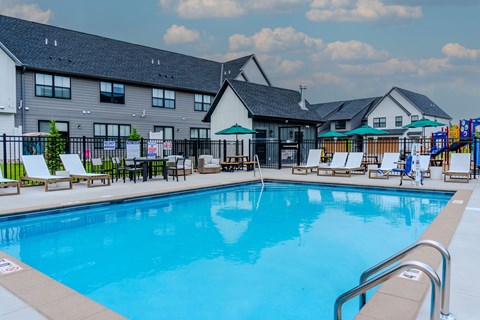 A large swimming pool in front of a building with a playground in the background.