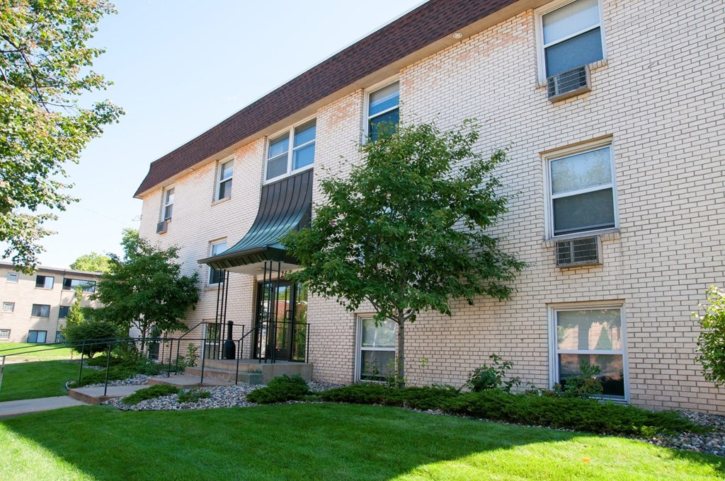 the exterior of a brick apartment building with a lawn and trees