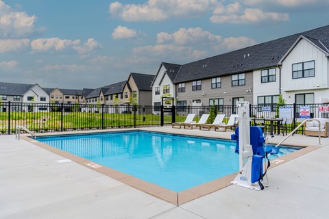 A swimming pool surrounded by a black fence and a blue lounge chair.