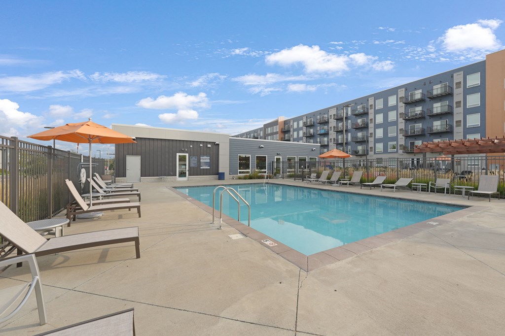 a swimming pool with chaise lounge chairs and umbrellas in front of a building