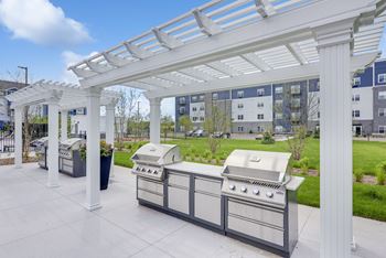 A white pergola is over a grill and table at Lochner Apartments, White Bear Lake
