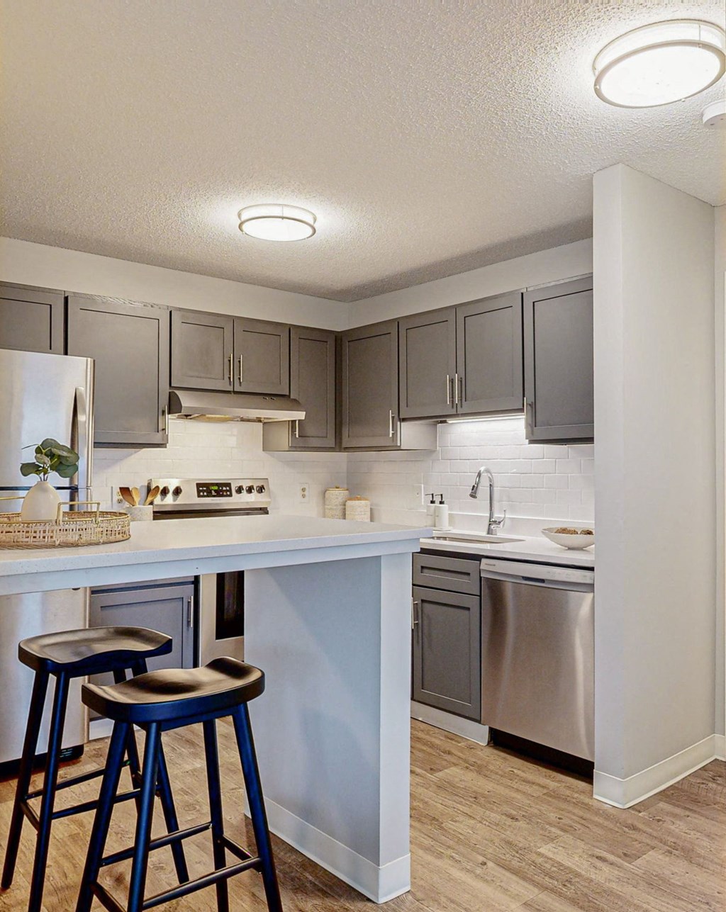 a kitchen with grey cabinets, white countertops and bar stools