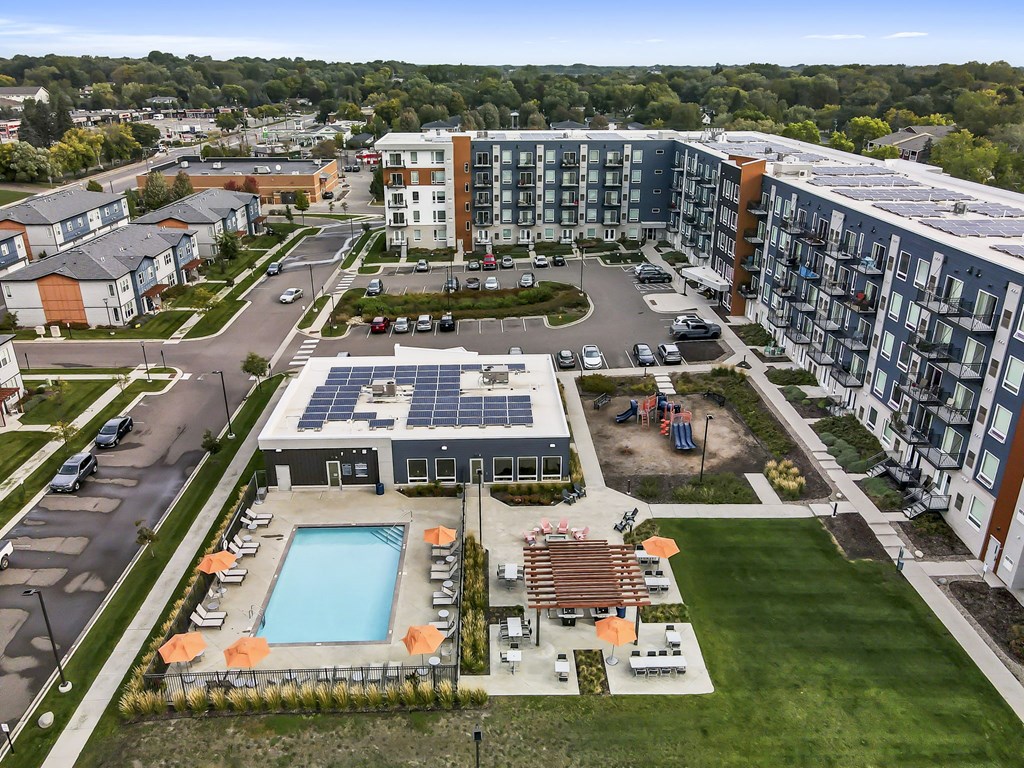 an aerial view of a building with a pool in the foreground and a parking lot in the