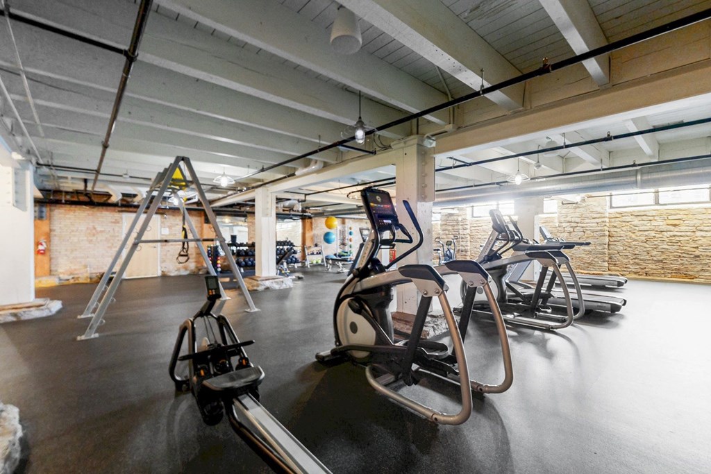 A gym with a row of treadmilers and elliptical machines.