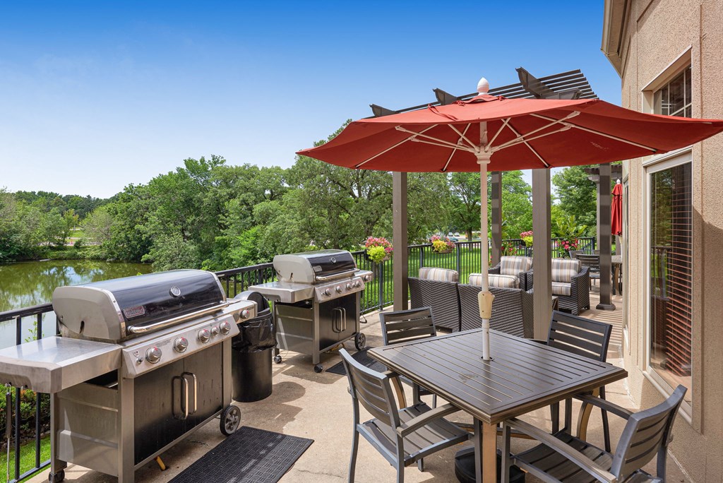 a patio with barbecue grills and tables with umbrellas