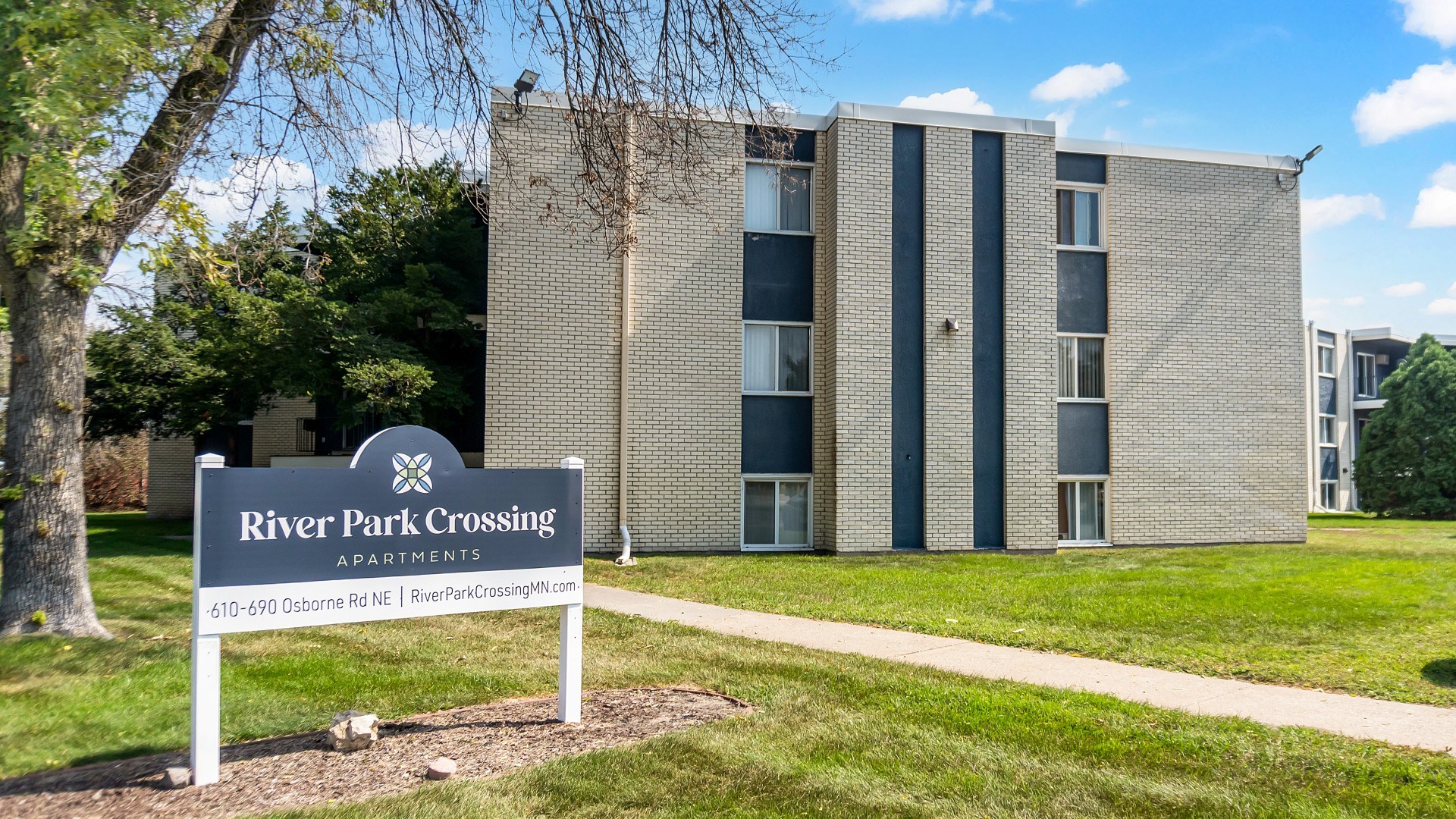 A sign for River Park Crossing Apartments stands in front of a building.