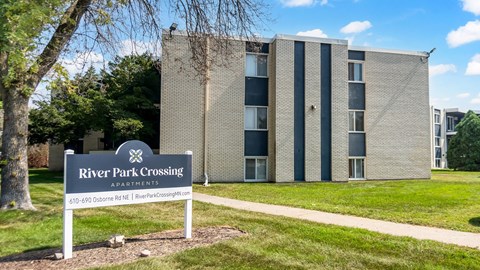 A sign for River Park Crossing Apartments stands in front of a building.