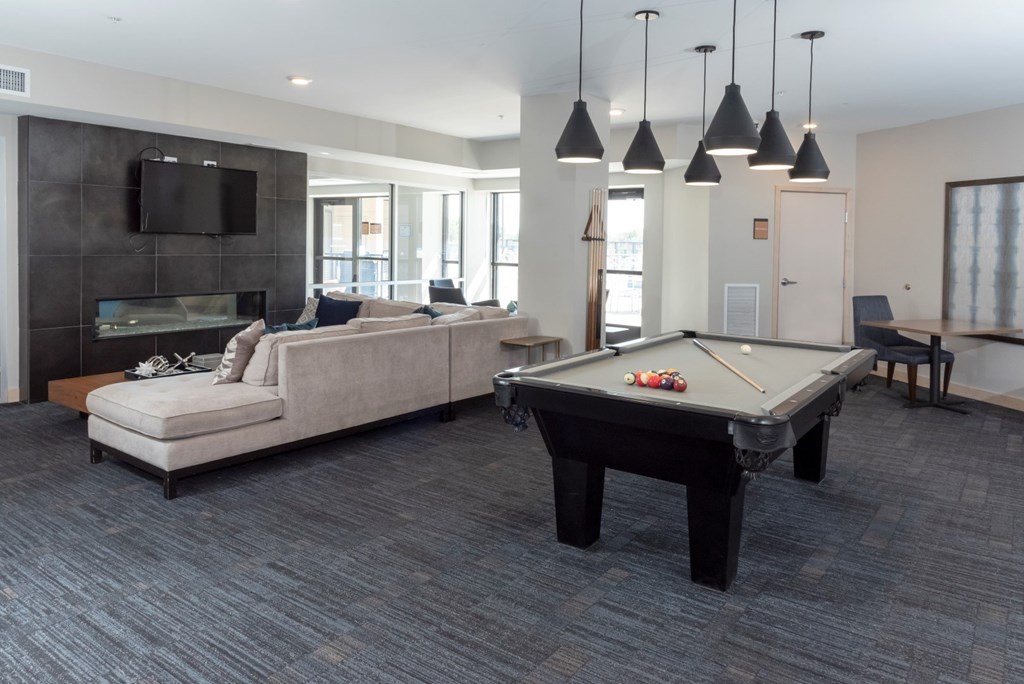 A billiard table is in the middle of a living room with a couch and a television.