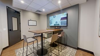 A conference room with a table, chairs, and a screen displaying a presentation. at Ardor on the Bluffs South Loop Residences Apartments, Minnesota, 55425