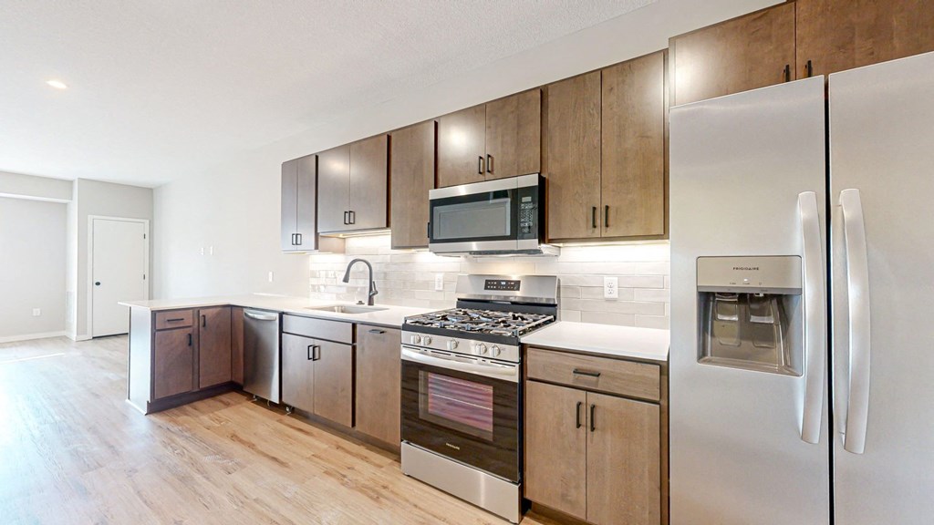 a kitchen with stainless steel appliances and wooden cabinets at Ardor on the Bluffs South Loop Residences Apartments, Bloomington