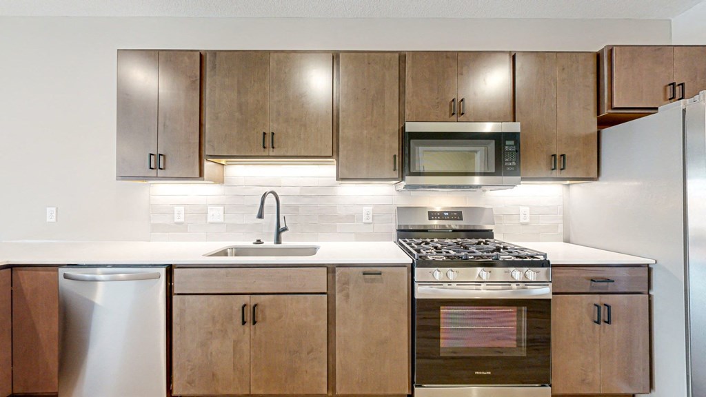 a kitchen with wooden cabinets and stainless steel appliances at Ardor on the Bluffs South Loop Residences Apartments, Bloomington, Minnesota