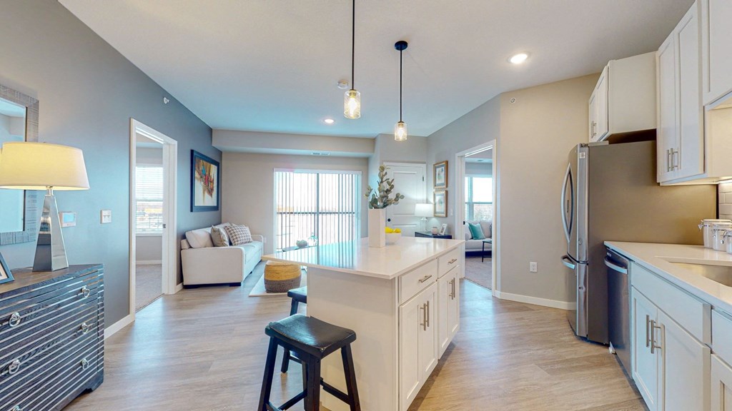 a kitchen with an island and stools in front of a living room with a couch and