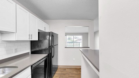 A black fridge in a kitchen with white cabinets and a window.
