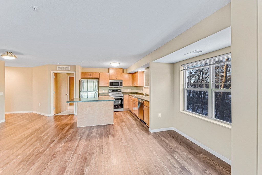 an empty living room and kitchen with wood floors and a large window