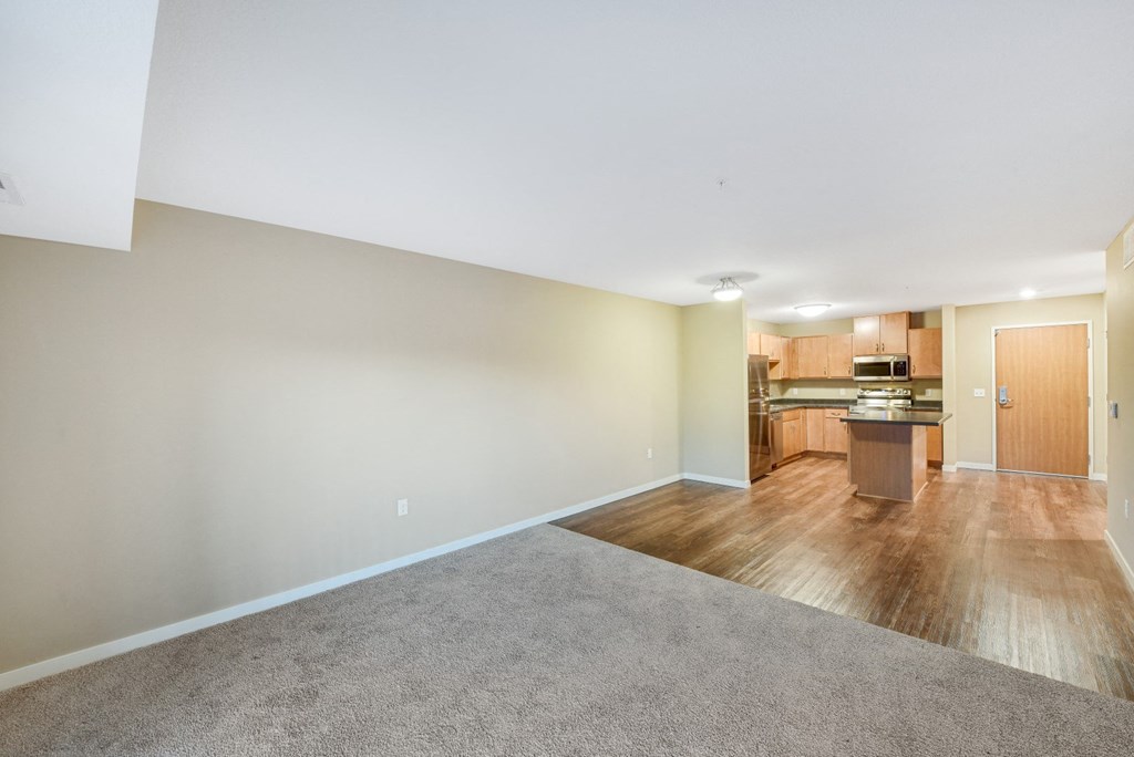 an empty living room with a kitchen in the background
