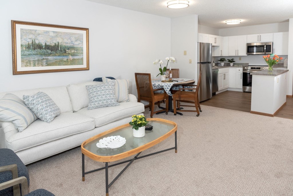 a living room with a couch coffee table and a kitchen in the background  at Briarcliff Apartments, a 55+ Community, Mahtomedi, MN