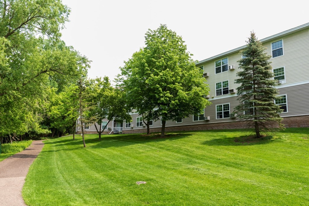 a grassy area with trees and a building in the background  at Briarcliff Apartments, a 55+ Community, Mahtomedi, MN, 55115