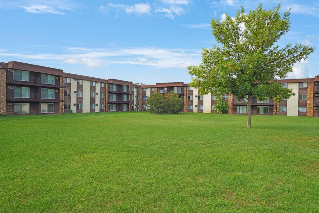 a grassy area with a tree in front of an apartment building
