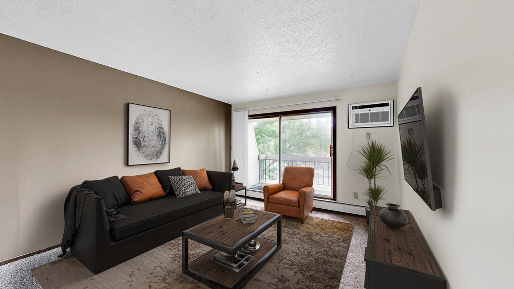A living room with a black couch, orange pillows, a coffee table, and a flat screen TV mounted on the wall.