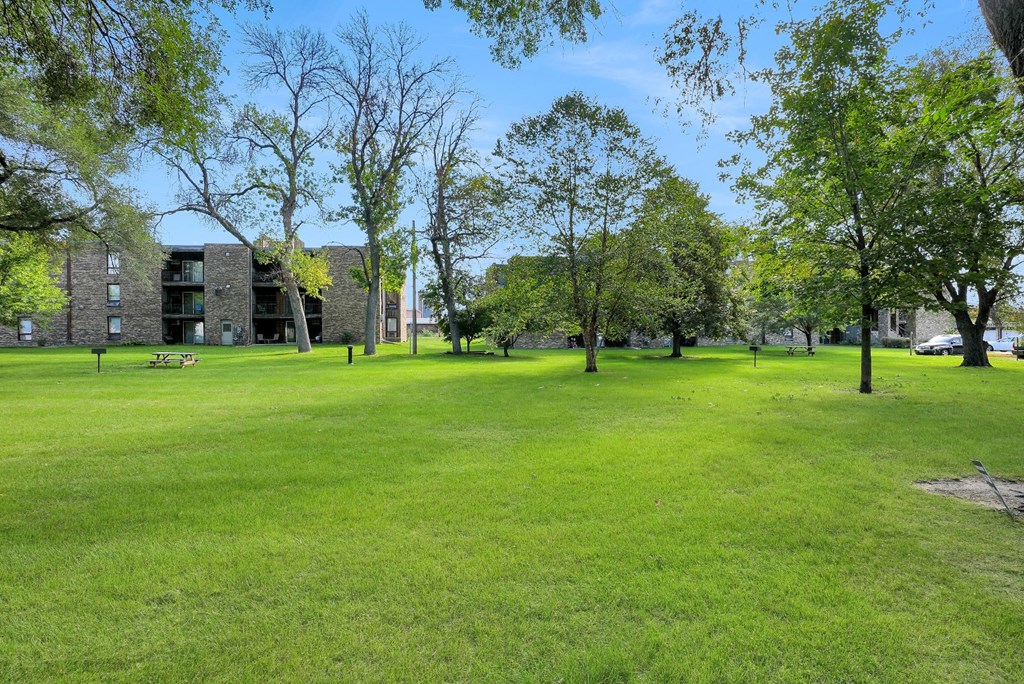 a large grassy field with trees in front of a building