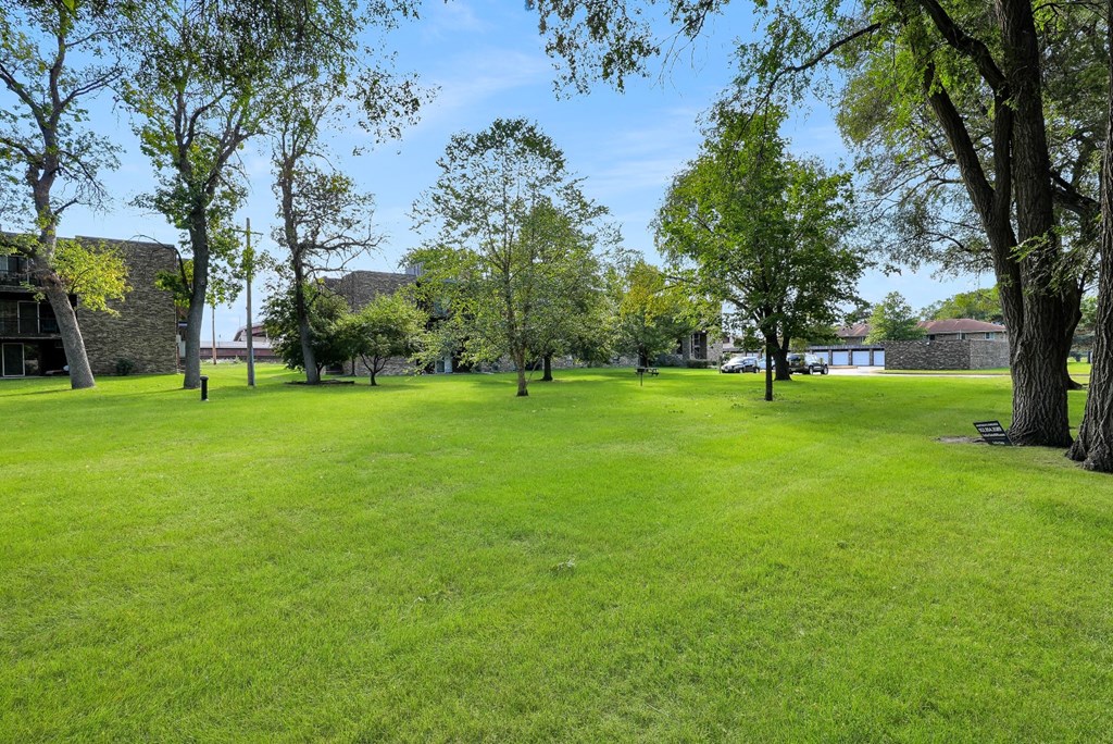 a large grass field with trees and buildings in the background