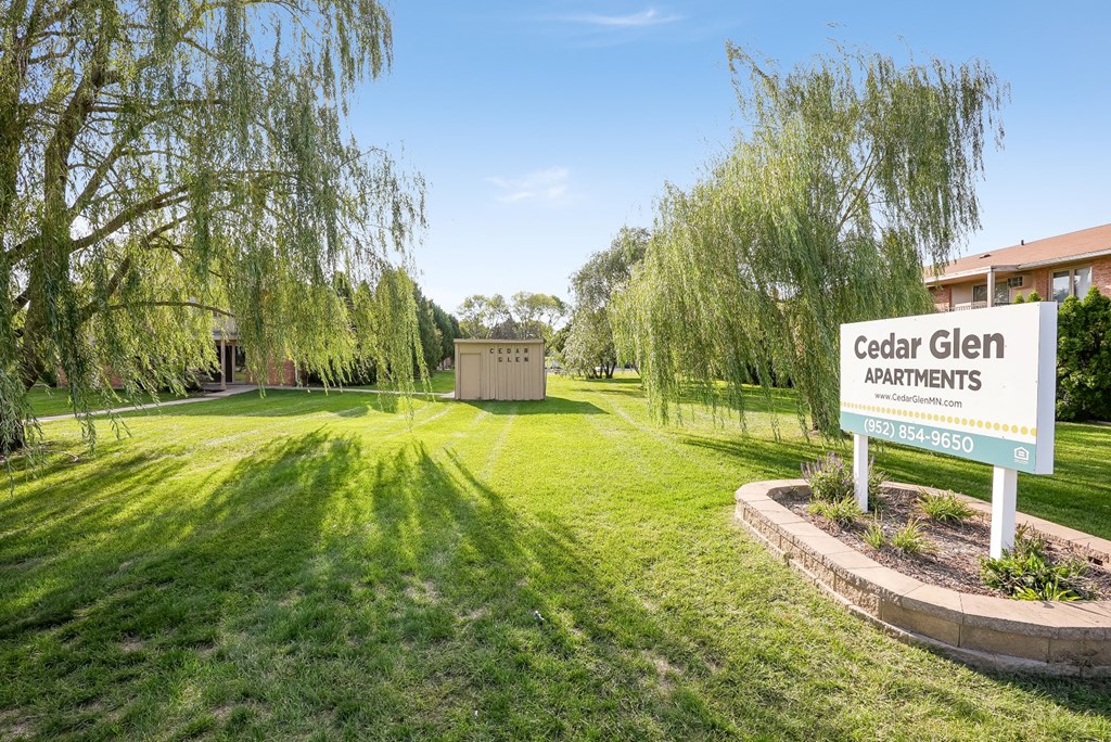 the sign for cedar glen apartments in front of a green field with trees