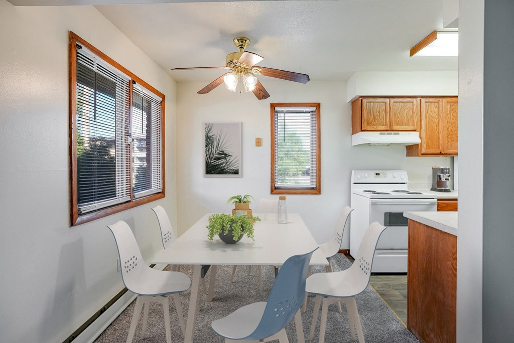 a dining room with a white table and chairs and a kitchen with a ceiling fan