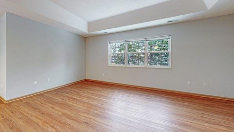A room with wooden flooring and a window with a view of trees.