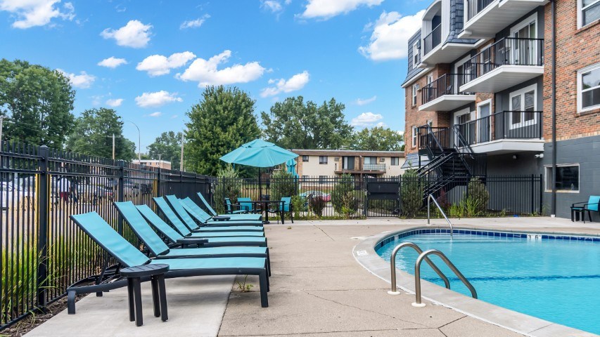 A pool area with a row of lounge chairs and a building in the background.