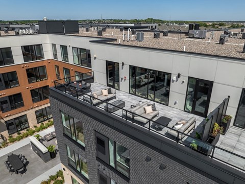 A rooftop patio with a table and chairs overlooks a cityscape.