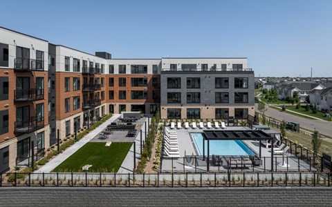 A modern apartment complex with a pool and a fenced-in parking area.