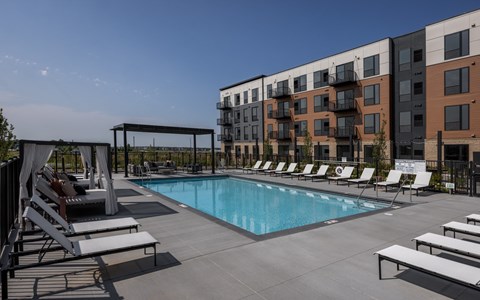 A pool area with sun loungers and a building in the background.